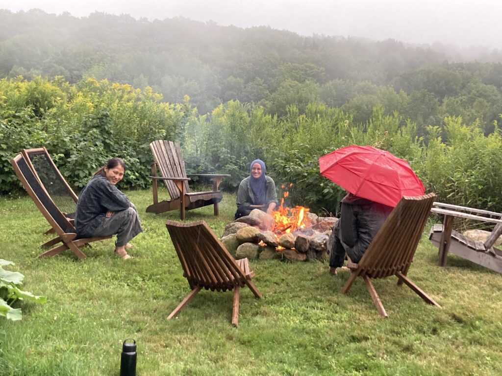 Artists in residents around a campfire in the rain.